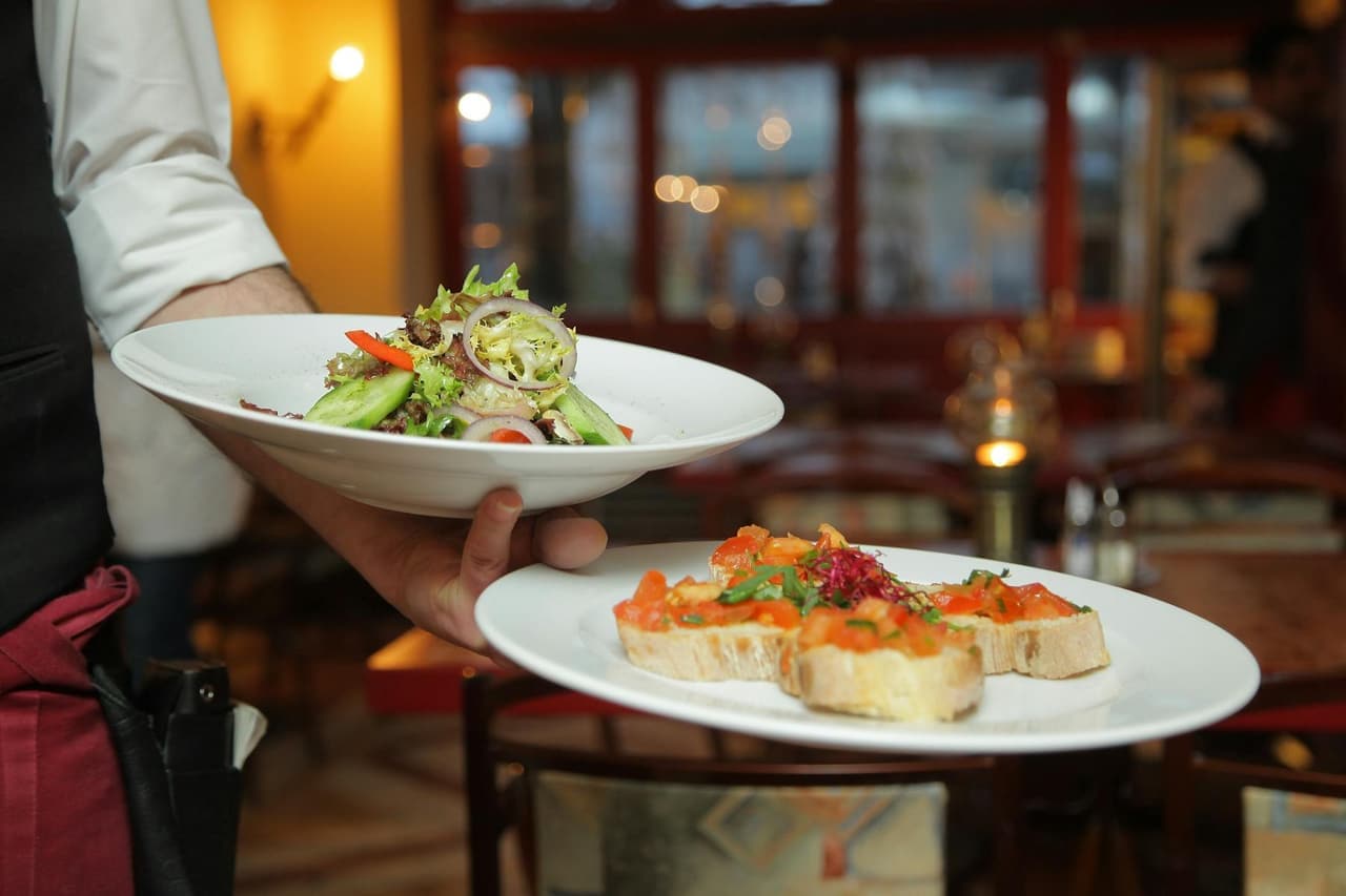 Server presenting plated dishes in a warmly lit dining room